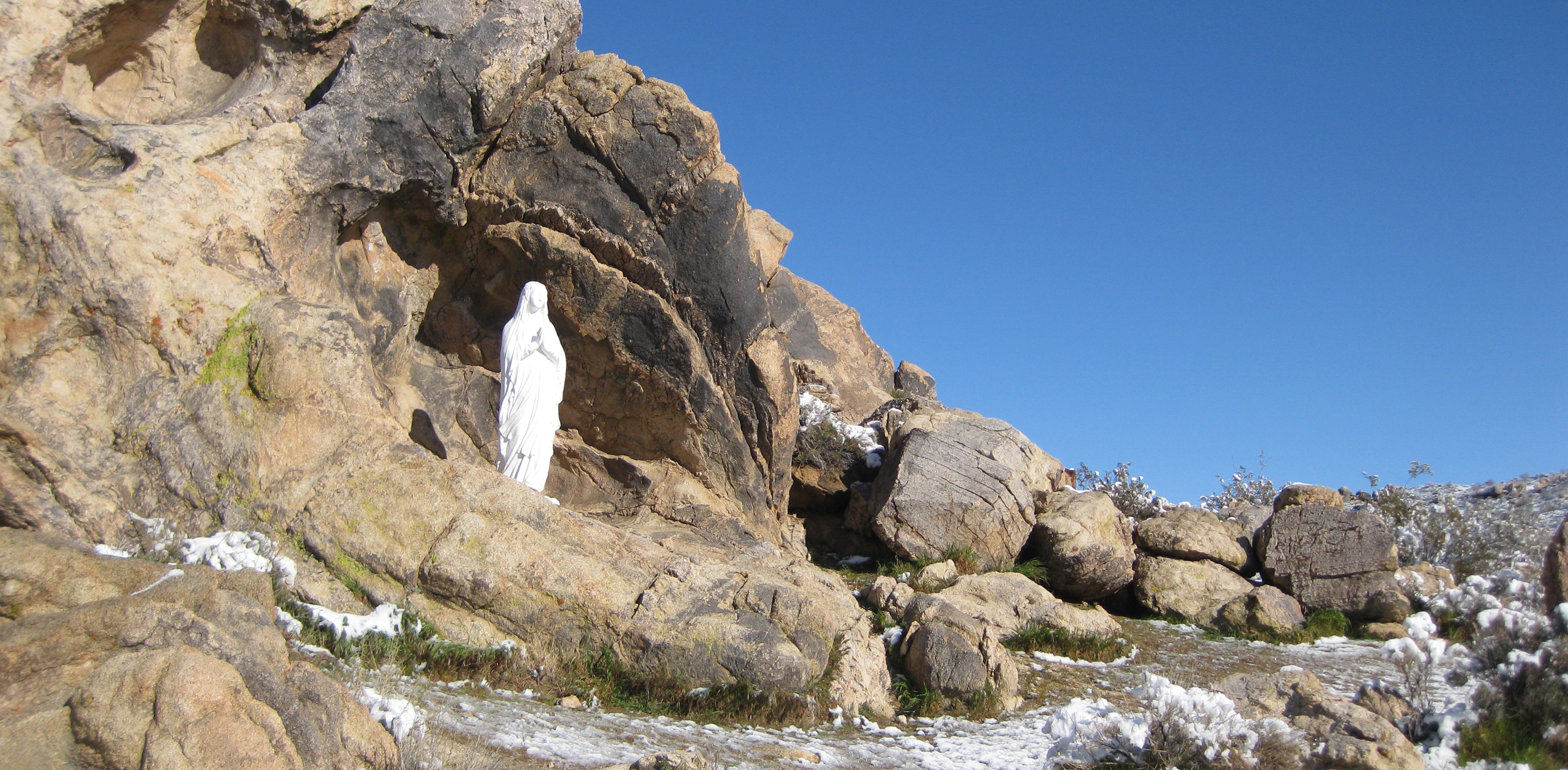 Statue of Mary in rock formation above flowing stream