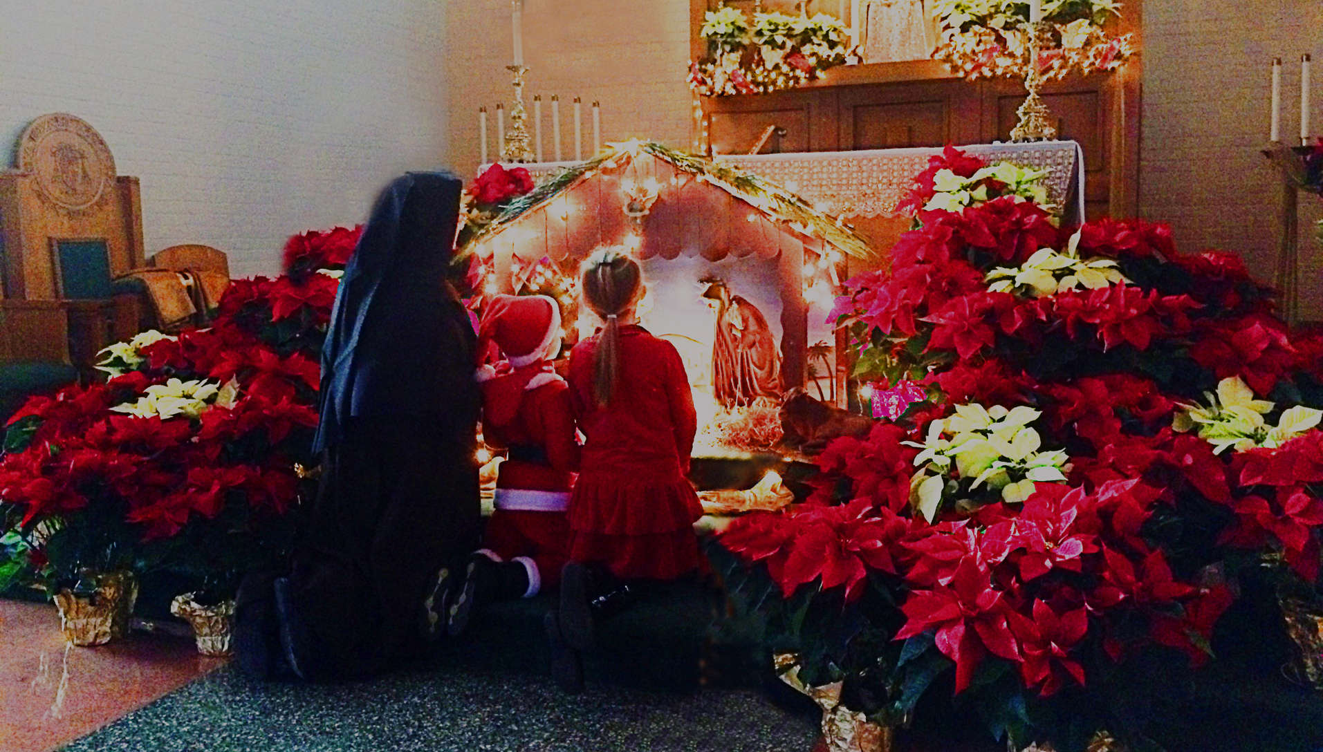 Sister and children kneeling in front of nativity scene