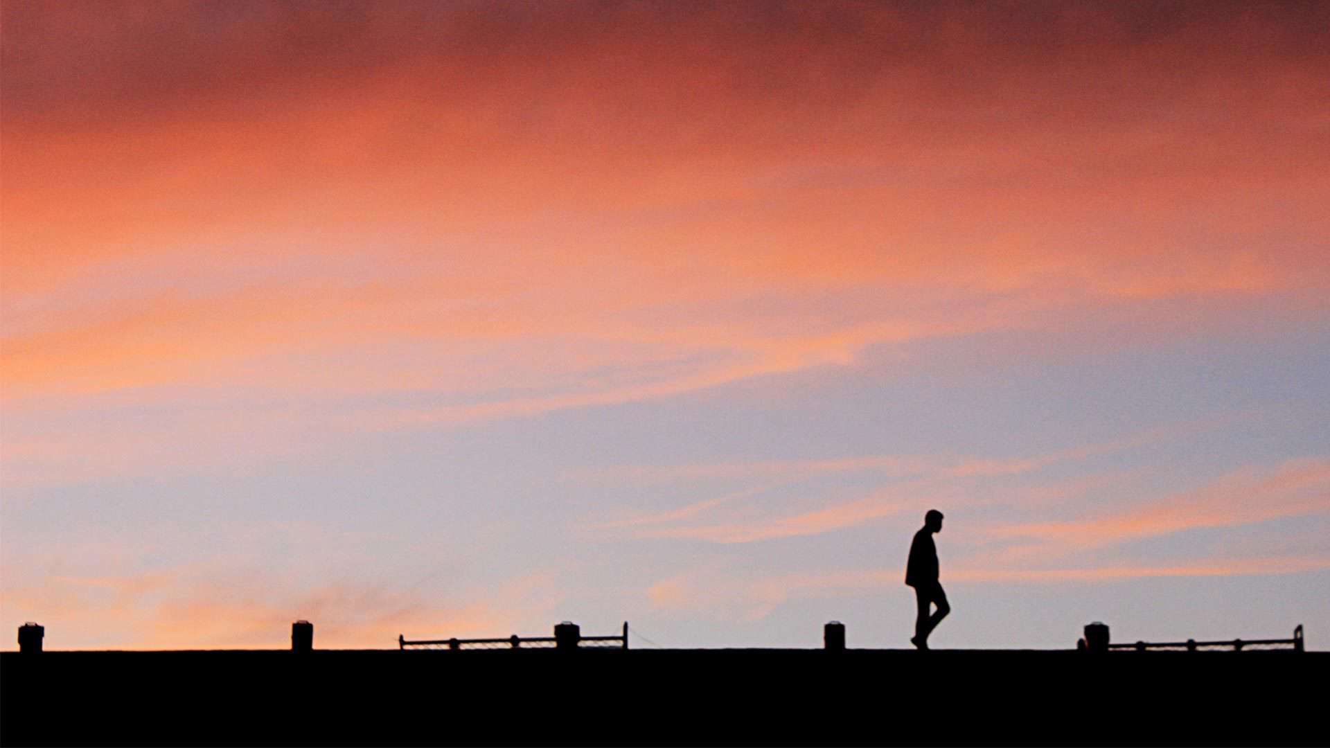 silhouette of man walking on roof with sunset behind him