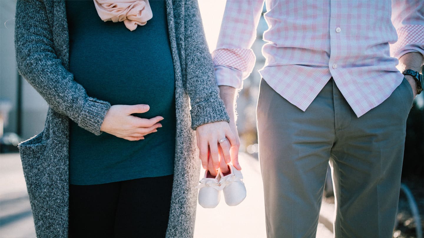 couple holding hands and baby shoes, wife is holding pregnant belly with other hand